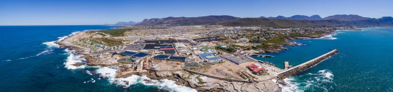 Luftaufnahme des New Harbour von Hermanus mit Hafenmauer, Fischereigebäuden und der Stadt vor den Bergen