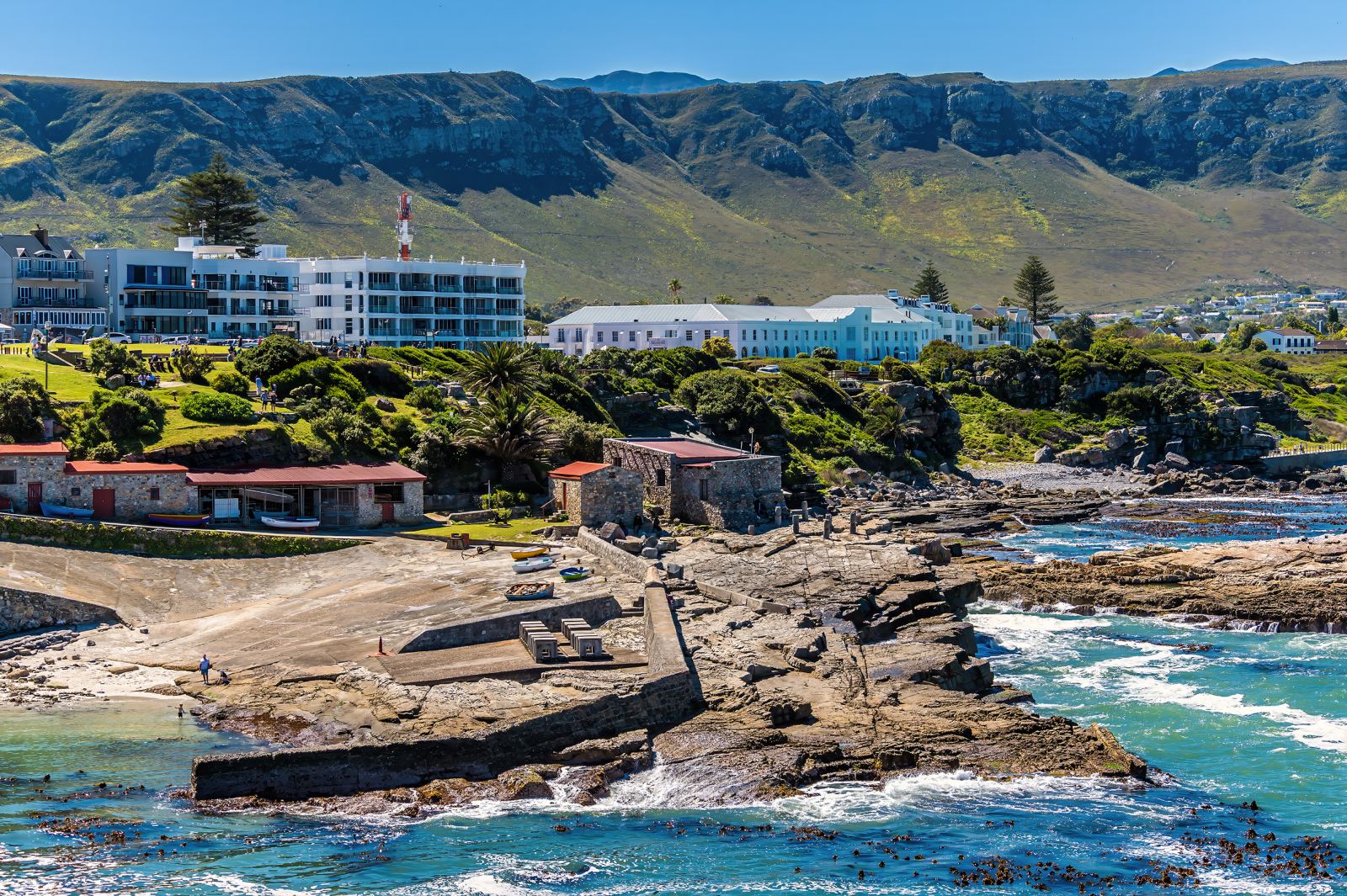 Der alte Hafen von Hermanus mit Slipanlage, Steinhäusern und Hotel vor den Bergen