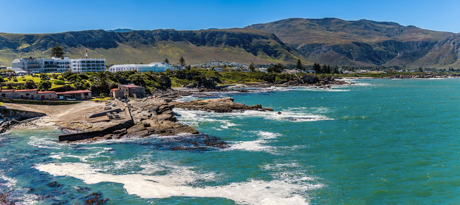 Panorama der Küste von Hermanus mit dem alten Hafen, Klippen und türkisfarbenem Wasser
