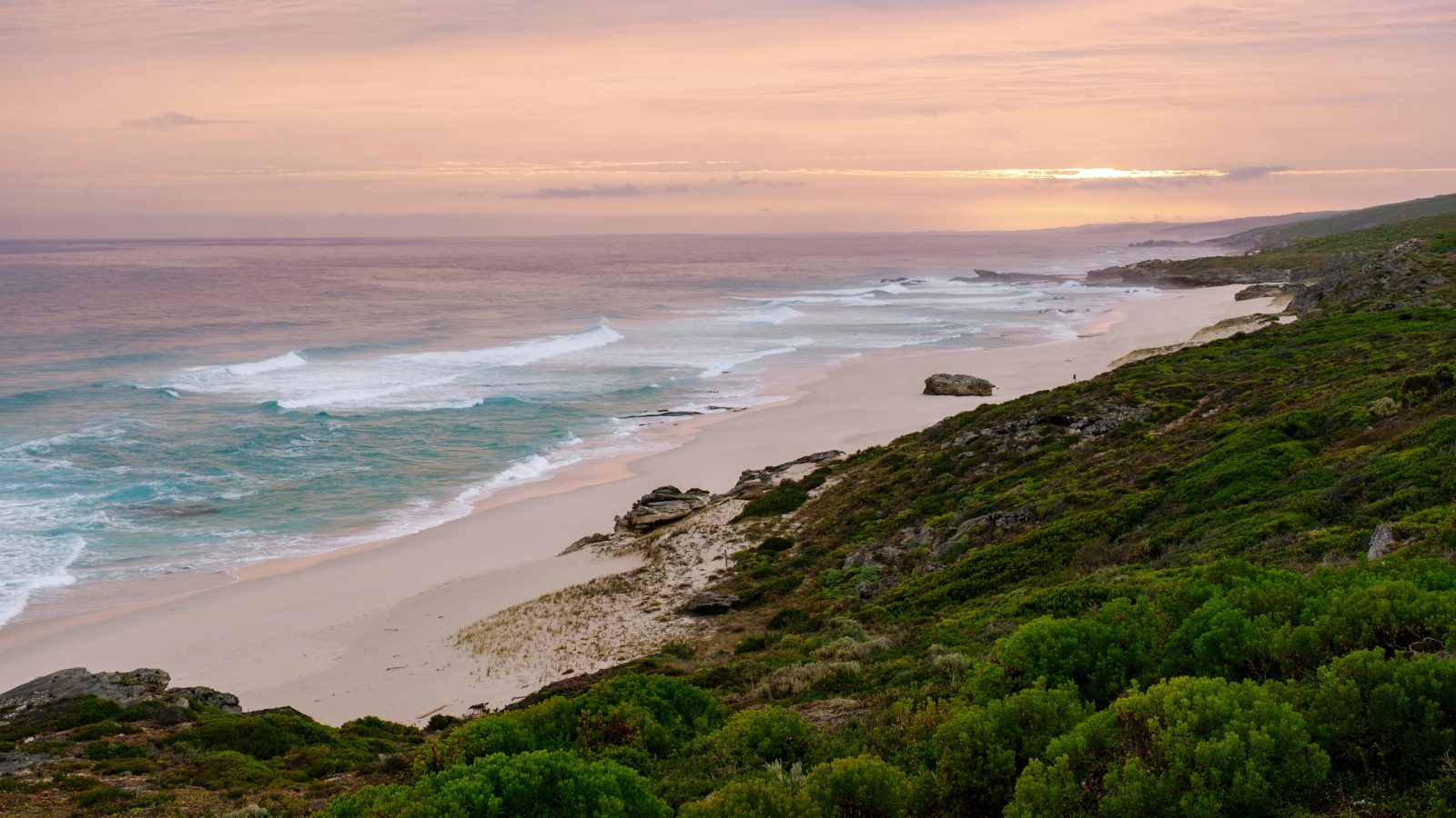 Langer Sandstrand bei Hermanus im Abendlicht, davor Fynbos, Wellen laufen aus